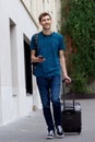 Full length happy young man traveling with suitcase and mobile phone on city street Royalty Free Stock Photo