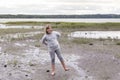 Full length horizontal shot of pretty smiling young girl standing on one foot on muddy beach Royalty Free Stock Photo