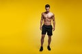 Full length image of a athletic man showing muscular body and sixpack abs, posing in studio, isolated yellow background.