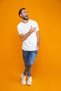 Full length image of bearded guy 30s in t-shirt and jeans pointing fingers aside while standing,  over yellow background Royalty Free Stock Photo