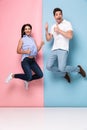 Full length image of cheerful man and woman in casual wear jumping and smiling together, isolated over colorful background Royalty Free Stock Photo