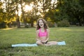 Full length image of a cute smiling little girl with curly hair in sport wear doing yoga on the roll mat in the park Royalty Free Stock Photo