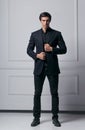 Full length image of an elegant fashion man adjusting his suit while looking at camera, on white background. Royalty Free Stock Photo