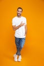 Full length image of joyous guy 30s in t-shirt and jeans pointing fingers aside while standing, over yellow background