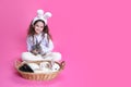 Full length of a smiling little girl with bunny ears, straw basket with little rabbits, isolated on a pink background. Royalty Free Stock Photo