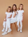 Full length image of three sisters with blond curly hair dressed in white clothes, isolated beige background Royalty Free Stock Photo