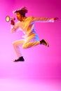 Full-length image of young boy jumping and emotionally shouting in megaphone against pink studio background in neon Royalty Free Stock Photo