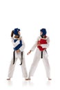 Full-length image of young competitive girls in dobok and helmet, practicing taekwondo, training isolated over white