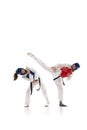 Full-length image of young competitive girls in dobok and helmet, practicing taekwondo, training isolated over white