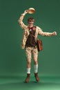 Full-length image of young guy in retro clothes in image of boy scout dancing, having fun against green studio Royalty Free Stock Photo