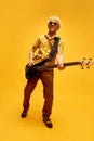 Full-length image of young smiling blonde man with curly hair in retro clothes playing guitar against yellow studio Royalty Free Stock Photo