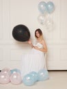 A full length image of a young smiling pregnant woman in anticipation of a baby in a white dress, hugs belly.