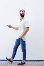 Full length laughing man with beard walking and holding cellphone