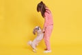 Full length of little girl playing with he pet, little dog standing on two legs, kid holding puppy`s paws in her hands and lookin Royalty Free Stock Photo