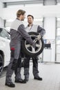 Full length of maintenance engineers carrying tire in car workshop Royalty Free Stock Photo