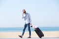 Full length man talking on cellphone with luggage on beach Royalty Free Stock Photo