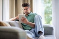 Full length of a mid aged man sitting on the couch at home and using digital tablet for work Royalty Free Stock Photo