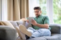 Full length of a mid aged man sitting on the couch at home and using digital tablet for work Royalty Free Stock Photo