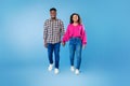 Full length of millennial African American couple walking, holding hands, smiling at camera on blue studio background Royalty Free Stock Photo