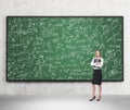 Full length of nice lady who holds black folder and stands in front of the green chalkboard.