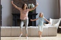 Full length overjoyed millennial mother dancing with little preschool daughter.