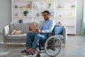 Full length of paraplegic black guy in wheelchair reading book at home