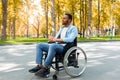 Full length of peaceful black handicapped guy in wheelchair having walk at urban park in autumn Royalty Free Stock Photo