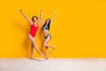 Full length photo of adorable carefree girls dressed swimsuits holding hands arms walking empty space isolated yellow