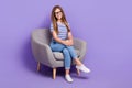 Full length photo of adorable intelligent girl wear striped t-shirt sit in armchair hands on knee on purple