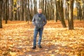 Full length photo of aged man walking along path in sunny golden forest. Fallen dry yellow maple leaves everywhere. Royalty Free Stock Photo