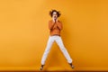 Full-length photo of amazed young woman in white pants dancing in studio. Portrait of wonderful girl with wavy hair