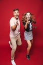 Full length photo of attractive man and woman in striped t-shirt jumping, while gesturing index fingers at you, isolated over red Royalty Free Stock Photo