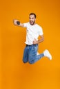 Full length photo of beautiful guy 30s in casual wear laughing and taking selfie on cell phone, isolated over yellow background Royalty Free Stock Photo