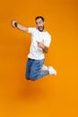 Full length photo of brunette guy 30s in casual wear laughing and taking selfie on cell phone, isolated over yellow background Royalty Free Stock Photo