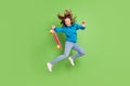 Full length photo of brunette ponytail haired girl jump wear jeans hold longboard fly hair isolated on green color