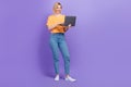 Full length photo cadre of cheerful young girl browsing her netbook searching more clients for sales isolated on purple