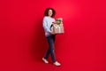 Full length photo of carefree pretty girl dressed ugly christmas sweater holding presents pile walking isolated red Royalty Free Stock Photo