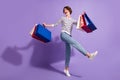 Full length photo of charming buyer lady dressed casual clothes dancing holding colorful bargains isolated purple color