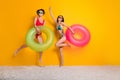 Full length photo of cheerful carefree girls dressed swimsuits jumping high holding inflatable circles empty space