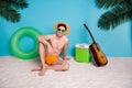 Full length photo of cheerful charming shirtless man straw hat sitting sand enjoying weekend  blue color Royalty Free Stock Photo