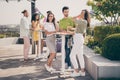 Full length photo of cheerful crowd of friends arms hold drink stand by table weekend gathering outdoors