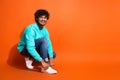 Full length photo of cheerful indian guy advertising new sneakers adidas brand lacing up sitting floor isolated on Royalty Free Stock Photo