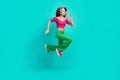 Full length photo of cool charming schoolgirl wear pink crop top flare trousers running jumping high isolated turquoise