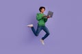 Full length photo of cool excited guy wear green pullover working modern gadget jumping empty space isolated purple