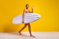 Full length photo of cool good mood shirtless man walking waving arm holding floating matrass yellow color