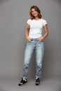 Full length photo of cute brunette woman with hands in her pockets wearing trendy mom jeans and white tshirt, looking at camera Royalty Free Stock Photo