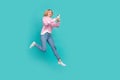 Full length photo of cute excited lady wear pink pullover texting modern device jumping empty space isolated turquoise