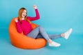 Full length photo of cute lucky young lady dressed pink outfit smiling sitting bean bag rising fists  blue color Royalty Free Stock Photo