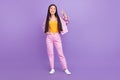 Full length photo of cute young brunette lady show v-sign wear jacket jeans sneakers isolated on violet background