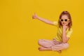 Full length photo of cute young girl dressed yellow T-shirt sitting floor thumb up with copy space isolated yellow color Royalty Free Stock Photo